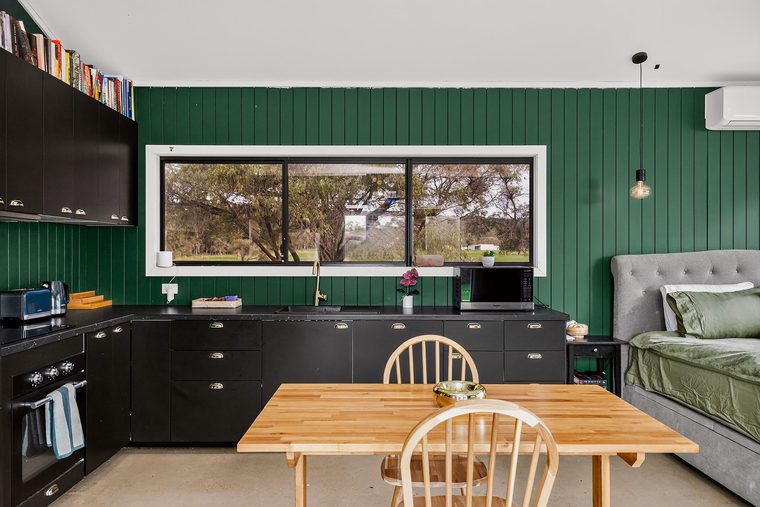 The black kitchen and timber dining table against forest green panelling